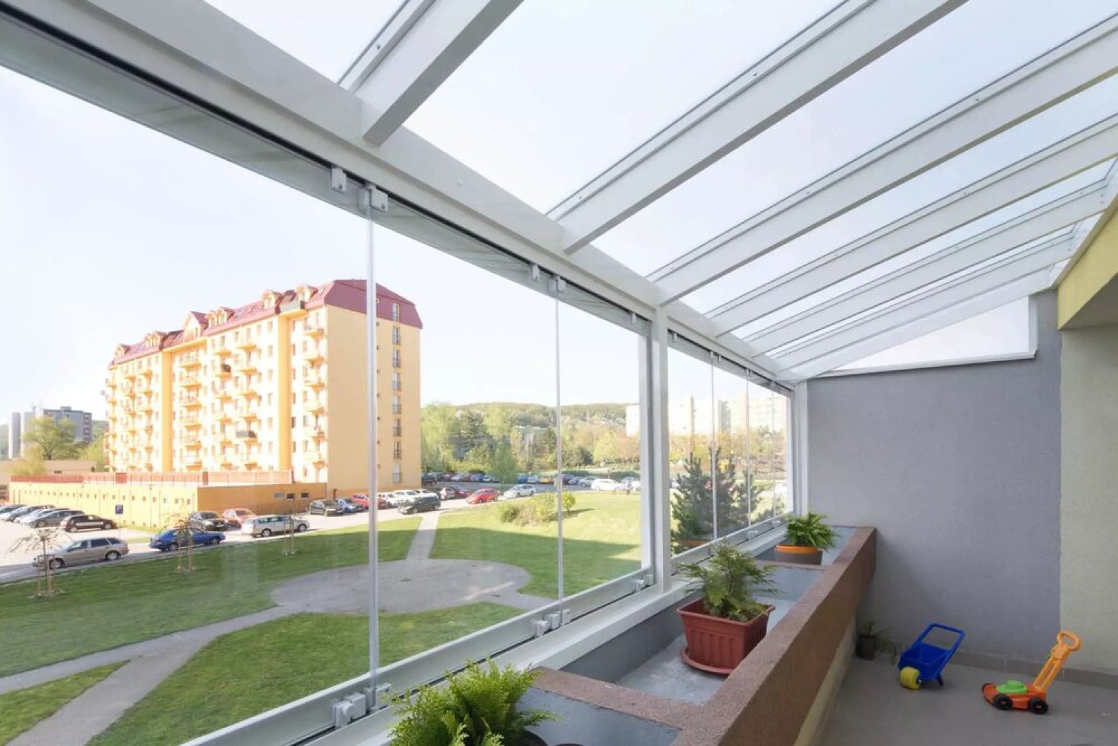 Moderní bezrámové zasklení balkonu s výhledem na sídliště a zeleň