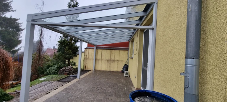 Moderní šedá hliníková pergola LIGHT se skleněnou střechou, připevněná ke zdi domu nad terasou