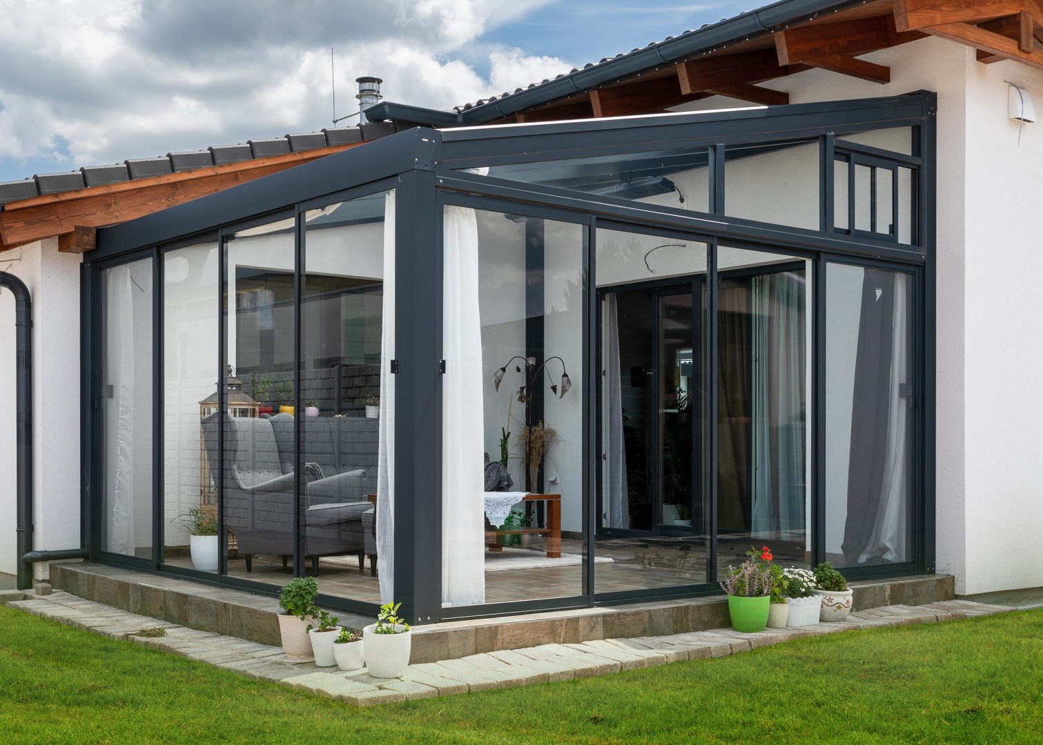 Moderní prosklená hliníková pergola připojená k domu s elegantním interiérovým nábytkem.
