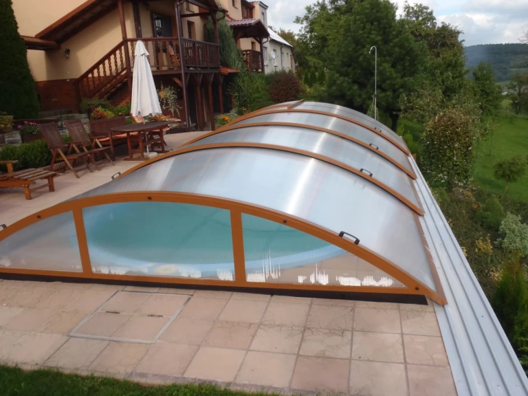 Uzavřená oblouková krytina bazénu KLASIK s hnědou konstrukcí v zahradě rodinného domu.