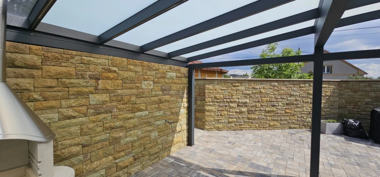 Moderní hliníková konstrukce zimní zahrady se zasklenou střechou vedle kamenné zdi