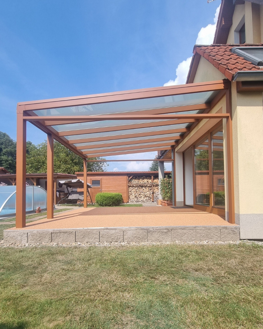 Hnědá hliníková pergola se skleněnou střechou, připojená k rodinnému domu
