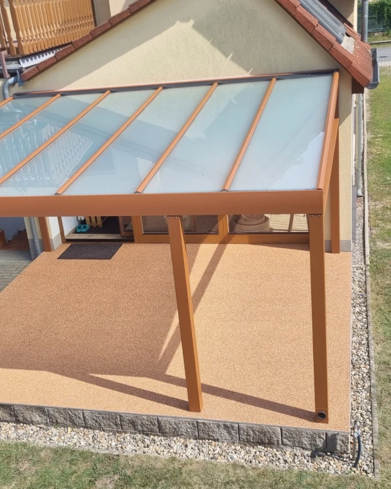 Moderní hliníková pergola s matným zasklením a hnědou konstrukcí, připevněná ke zdi domu