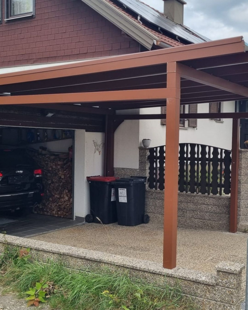Hnědý přístřešek pro auto vedle rodinného domu s garáží a odpadkovými koši