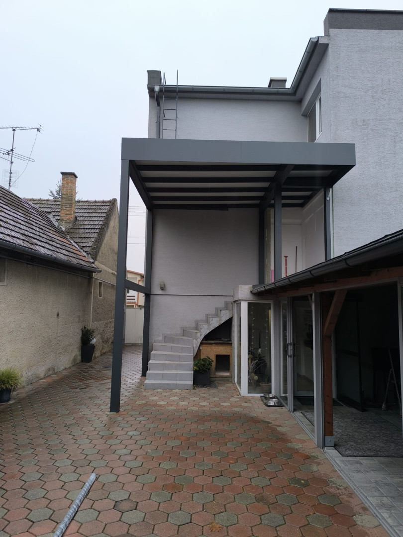 Moderní šedá hliníková pergola vyrobená na míru, instalovaná na terase rodinného domu nad venkovním schodištěm.