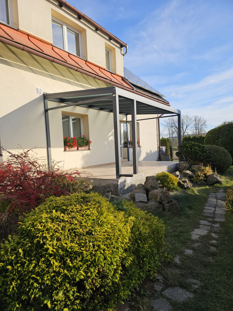 Moderní hliníková pergola se zasklenou střechou přistavěná k rodinnému domu se zahradou.