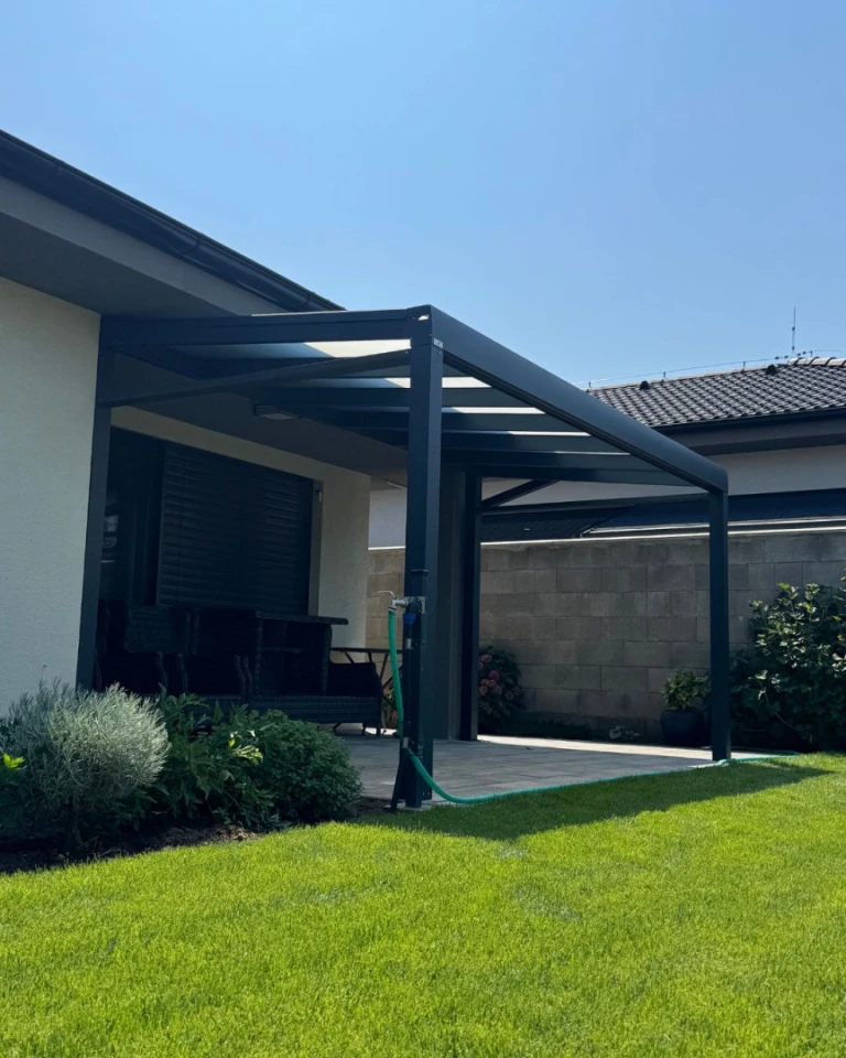 Moderní tmavě šedá hliníková pergola se skleněnou střechou přistavěná k rodinnému domu se zahradou