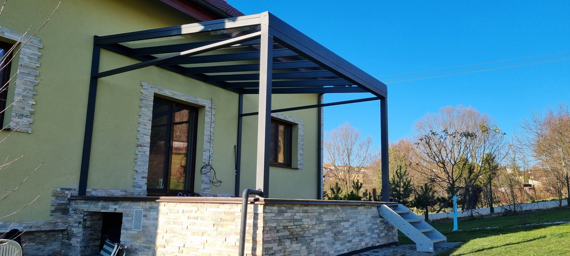 Moderní tmavě šedá hliníková pergola ROBUST se skleněnou střechou, namontovaná na terase rodinného domu.