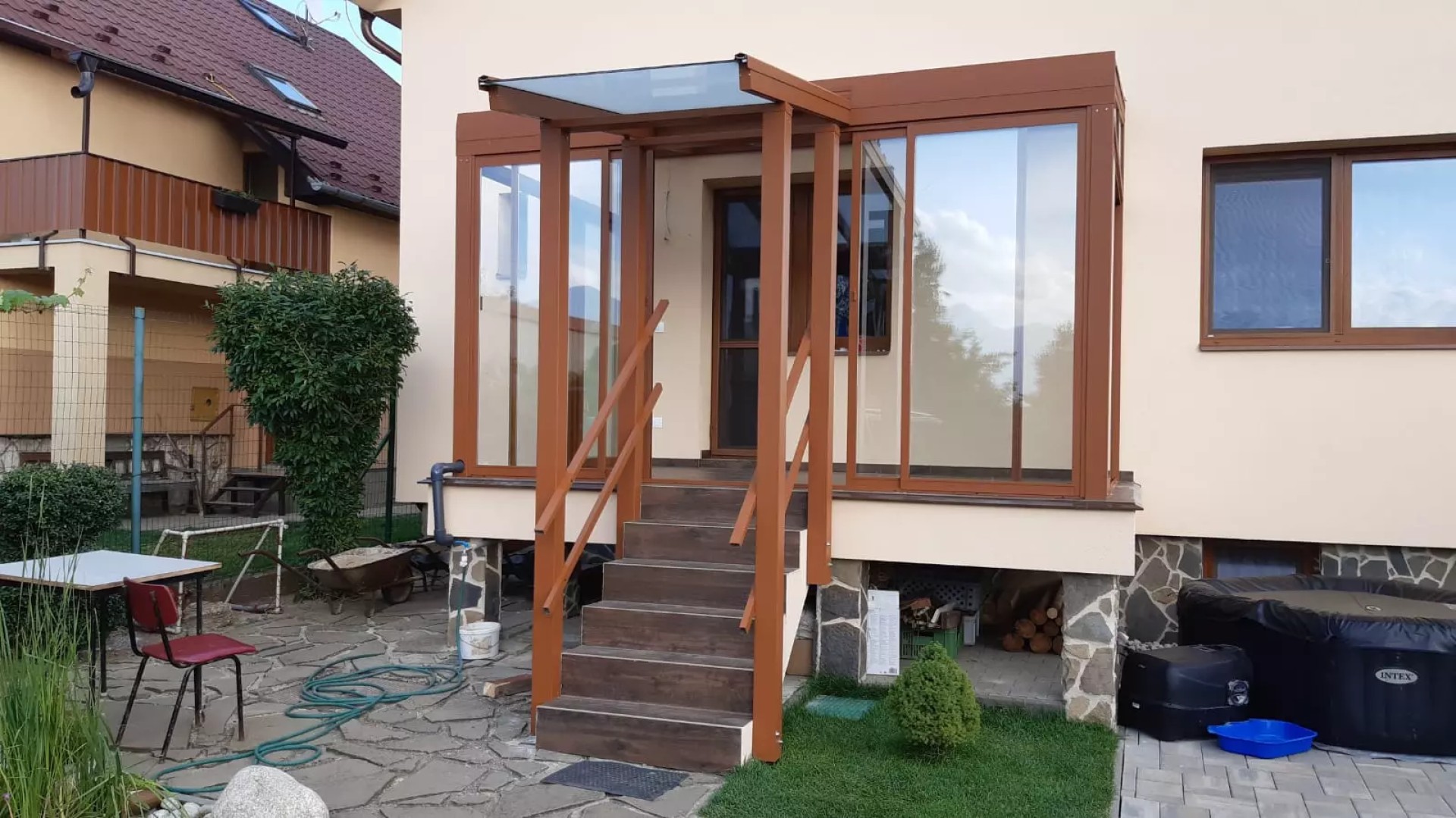 Hnědá prosklená hliníková pergola s přístřeškem nad vstupními schody u rodinného domu.