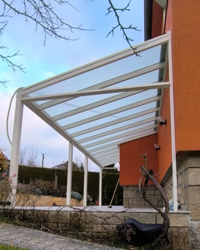 Moderní bílá hliníková pergola se skleněnou střechou připojená k oranžovému rodinnému domu