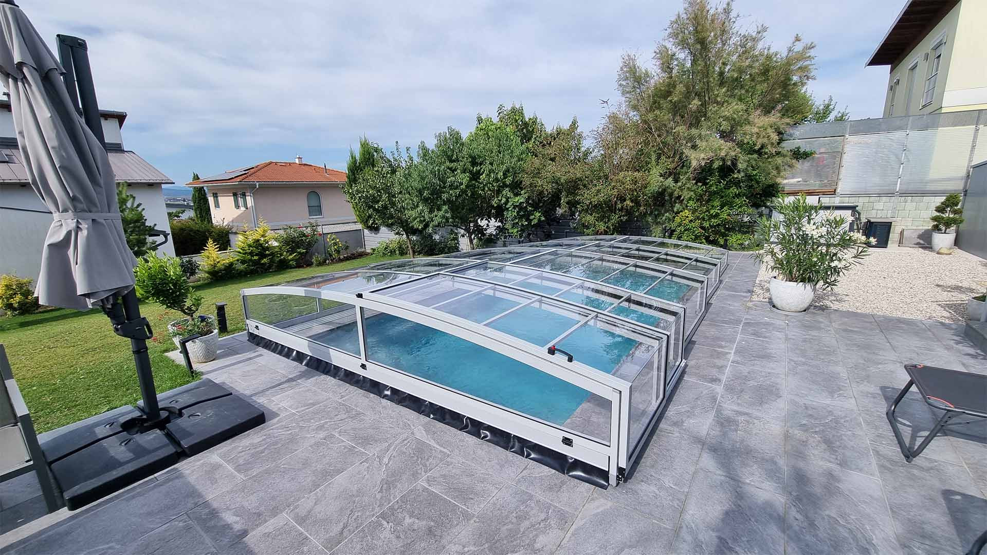 Moderní nízká hliníková střecha nad bazénem PREMIER na dlážděné terase v zahradě rodinného domu