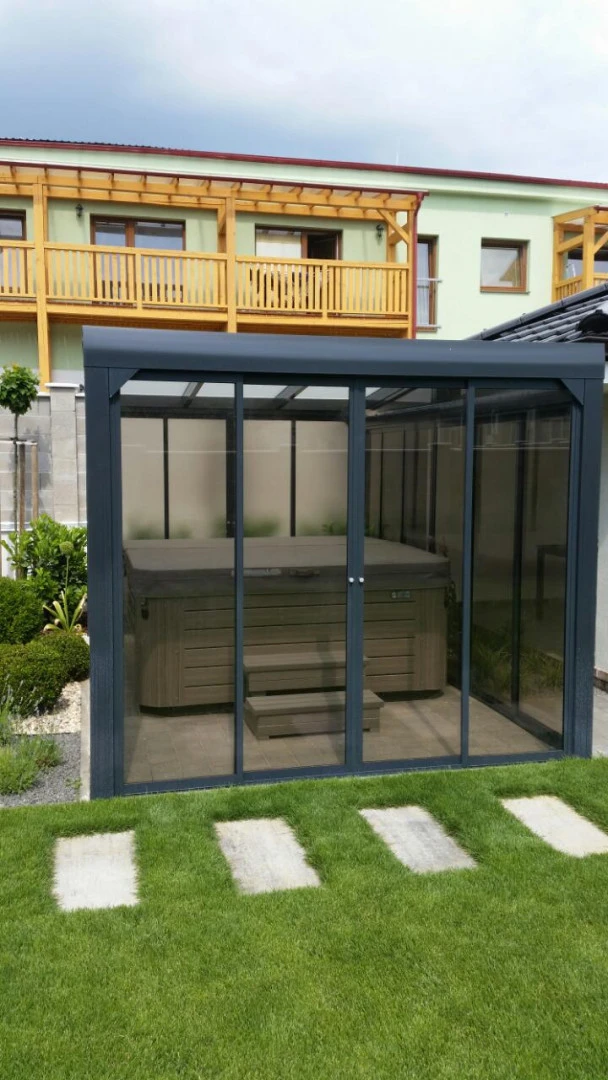 Moderní prosklený přístřešek s vířivkou umístěný v zahradě rodinného domu.