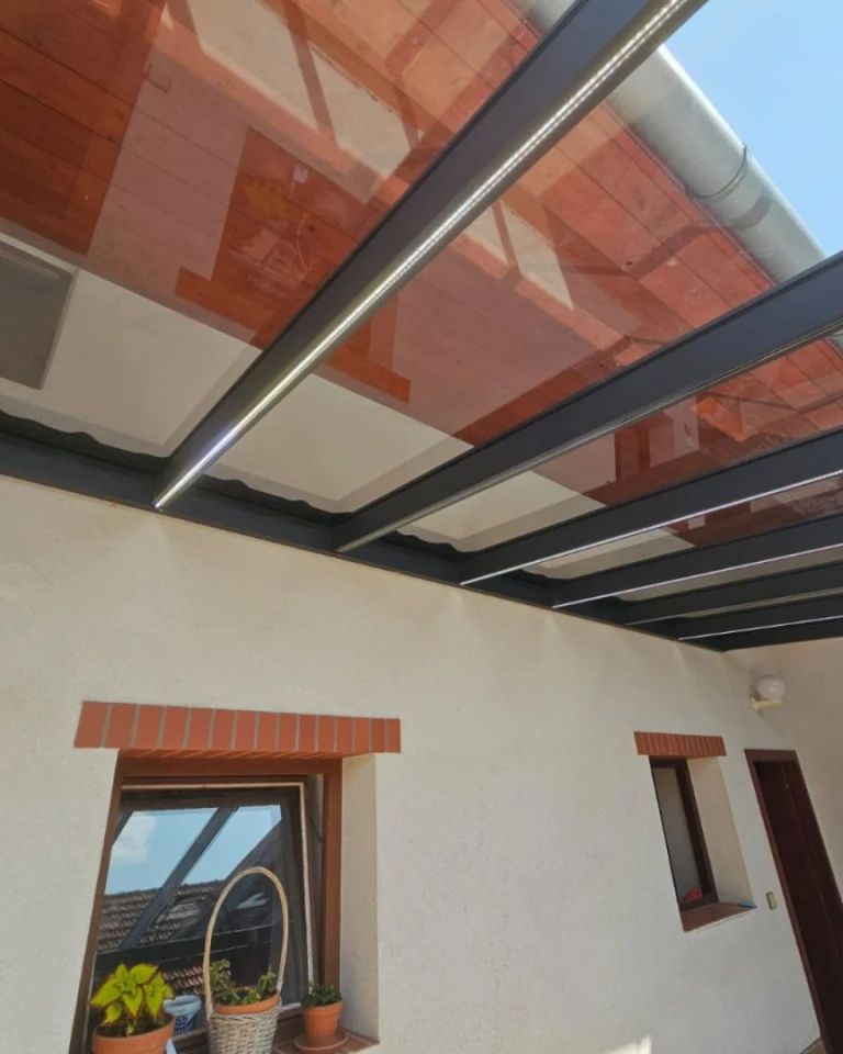 Detailní pohled na zastřešení hliníkové pergoly s integrovaným LED osvětlením, připevněné k fasádě domu.