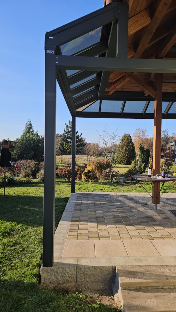 Detailní pohled na hliníkovou konstrukci a prosklenou střechu pergoly s výhledem do zahrady.