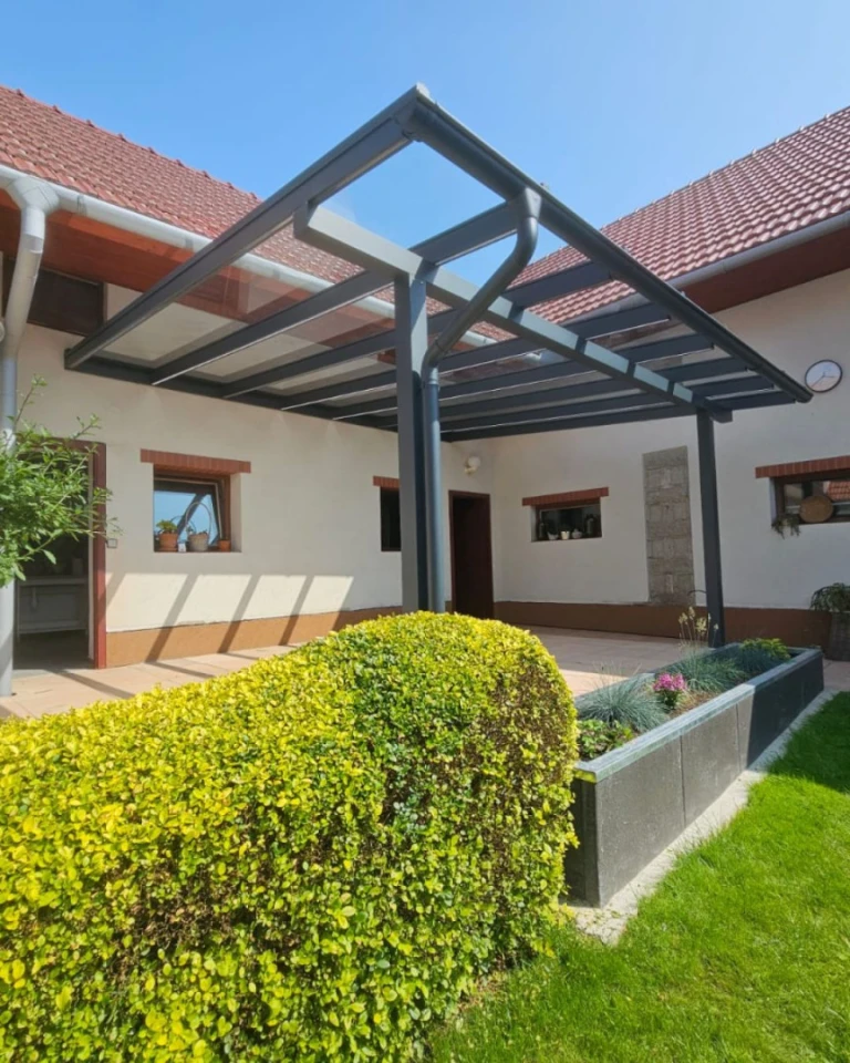 Moderní hliníková pergola se skleněnou střechou, připojená k rodinnému domu s upravenou zahradou.