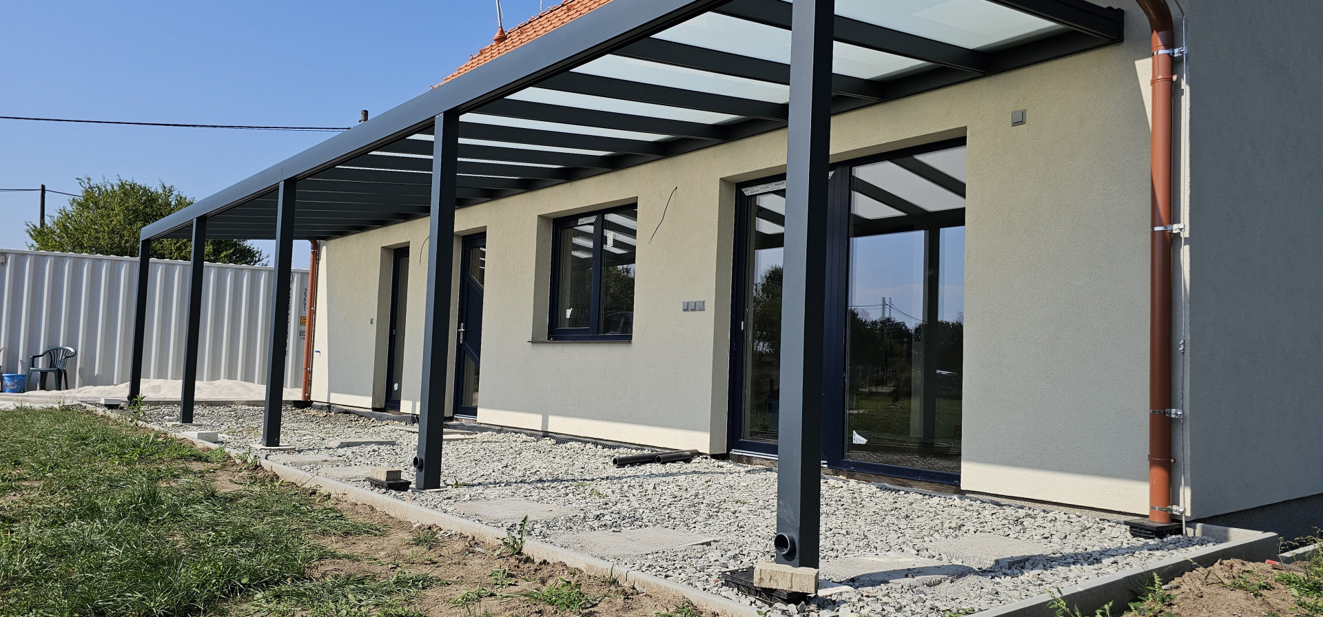Moderní hliníková pergola se skleněnou střechou připevněná ke zdi rodinného domu