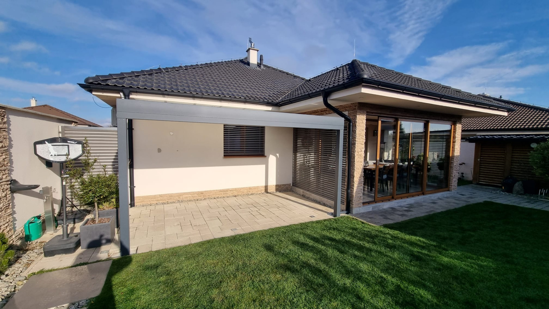 Moderní šedá hliníková pergola u bungalovu na dlážděné terase u zahrady