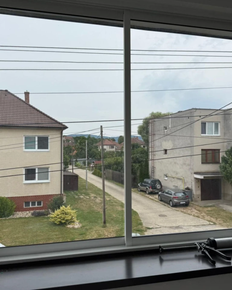 Pohled přes nové zasklení na ulici s rodinnými domy a auty ve Skalici.
