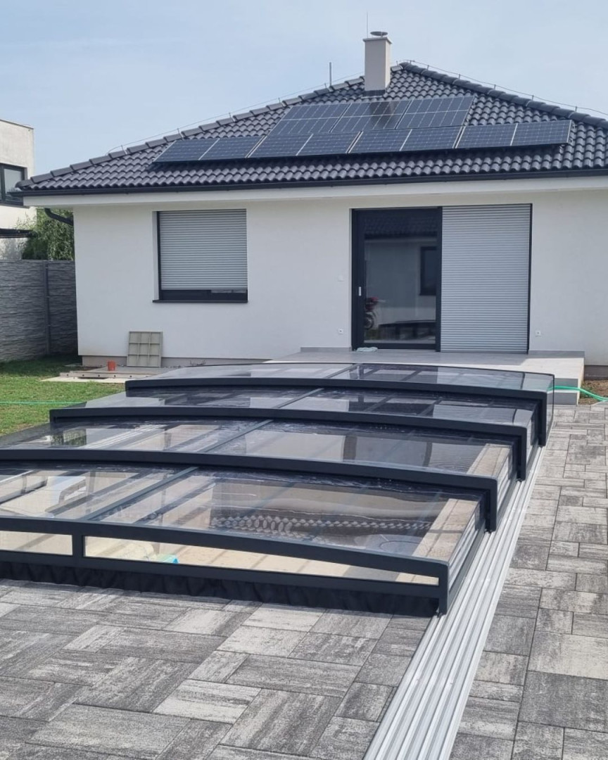 Moderní nízká krytina bazénu v antracitové barvě před rodinným domem s dlažbou a fotovoltaickým systémem.
