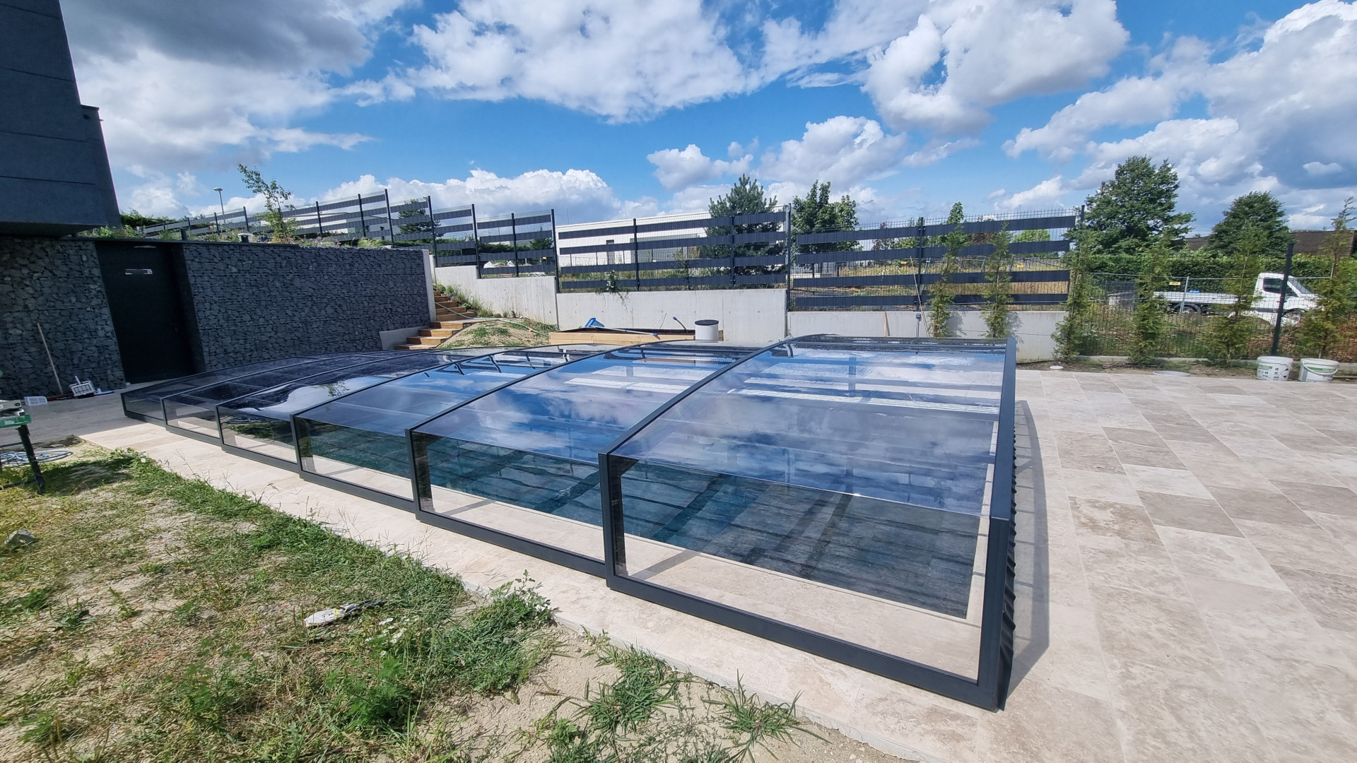 Moderní nízká zastřešení bazénu s tmavými profily a čirým výplňovým materiálem na terase rodinného domu