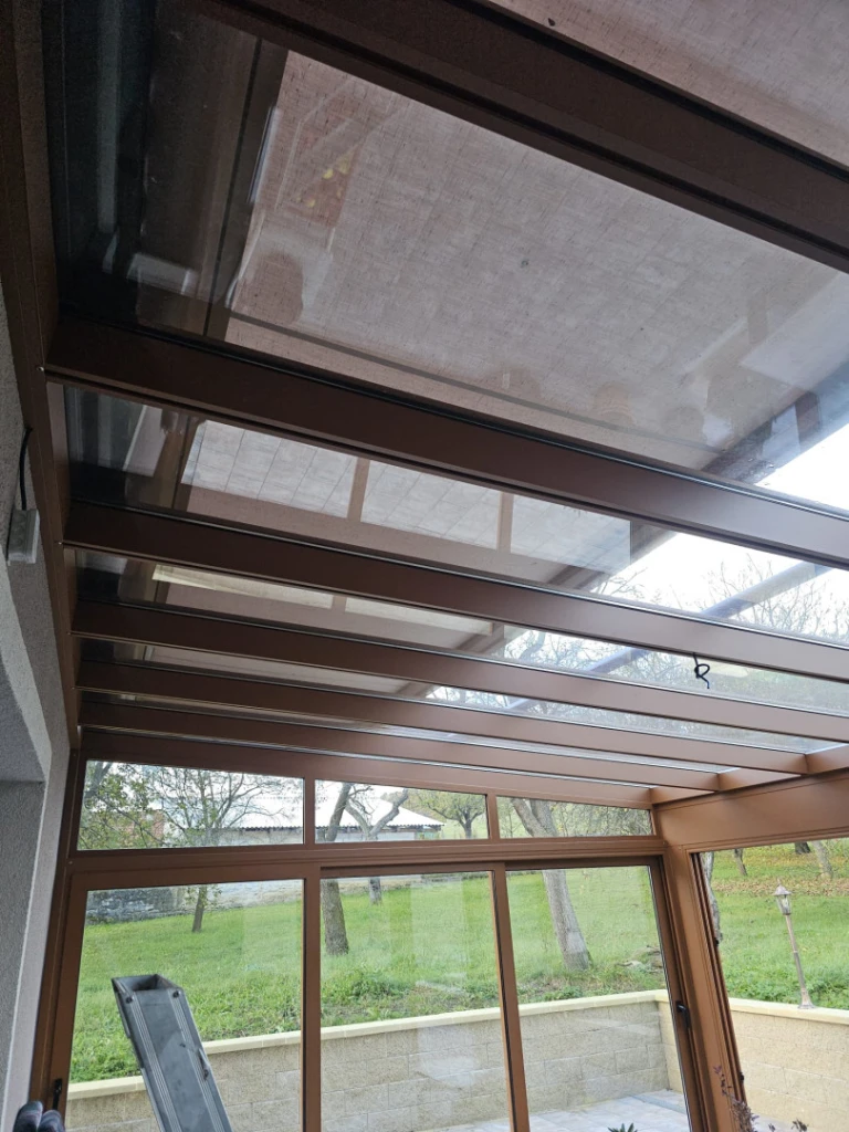 Detailní pohled na prosklenou střechu a konstrukci moderní zimní zahrady v hnědém provedení.