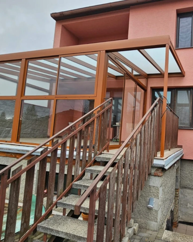 Hnědá prosklená hliníková pergola namontovaná na terase domu se schodištěm