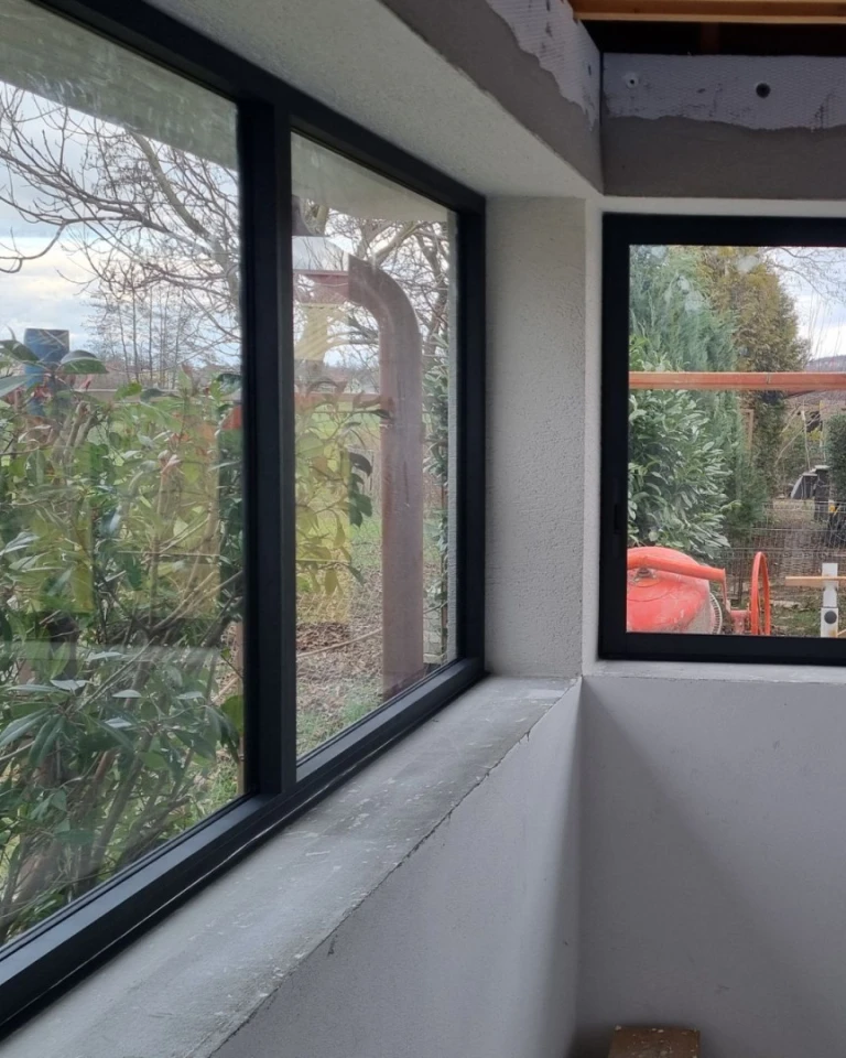 Detailní pohled na černý rám prosklené terasy v rohu místnosti s výhledem do zahrady.