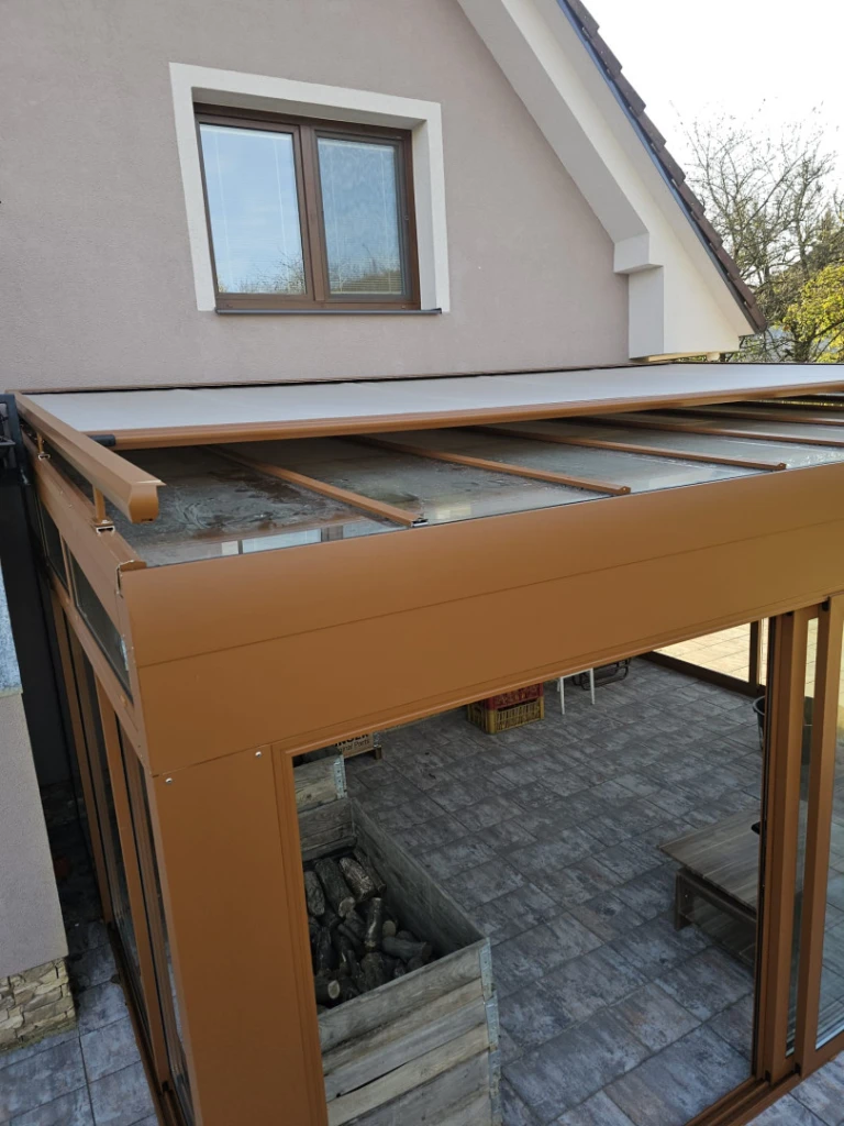 Moderní hnědá zimní zahrada se skleněnou střechou a vnějším stíněním na terase rodinného domu.