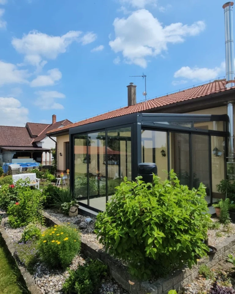 Moderní prosklená zimní zahrada s antracitovou konstrukcí u rodinného domu s udržovanou zahradou